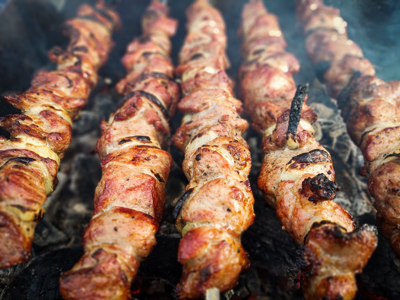 Pork souvlaki skewers grilling over charcoal.
